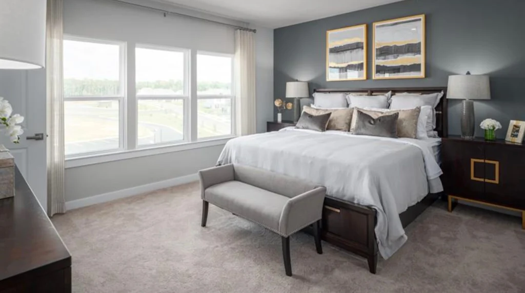 Bright bedroom with a wall of windows, an upholstered bench at the foot of the bed and framed art