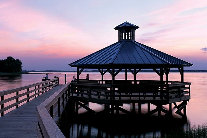 A gazebo at the end of a wooden pier over the water at dusk
