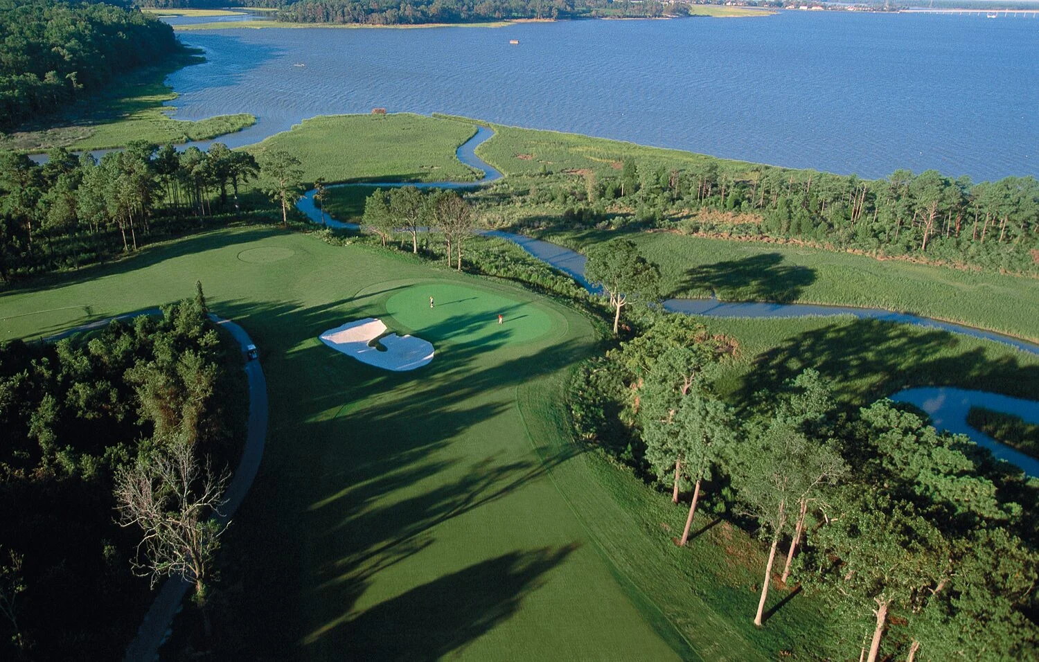 Aerial view of a golf course winding through tidal wetlands and pines beside a wide river