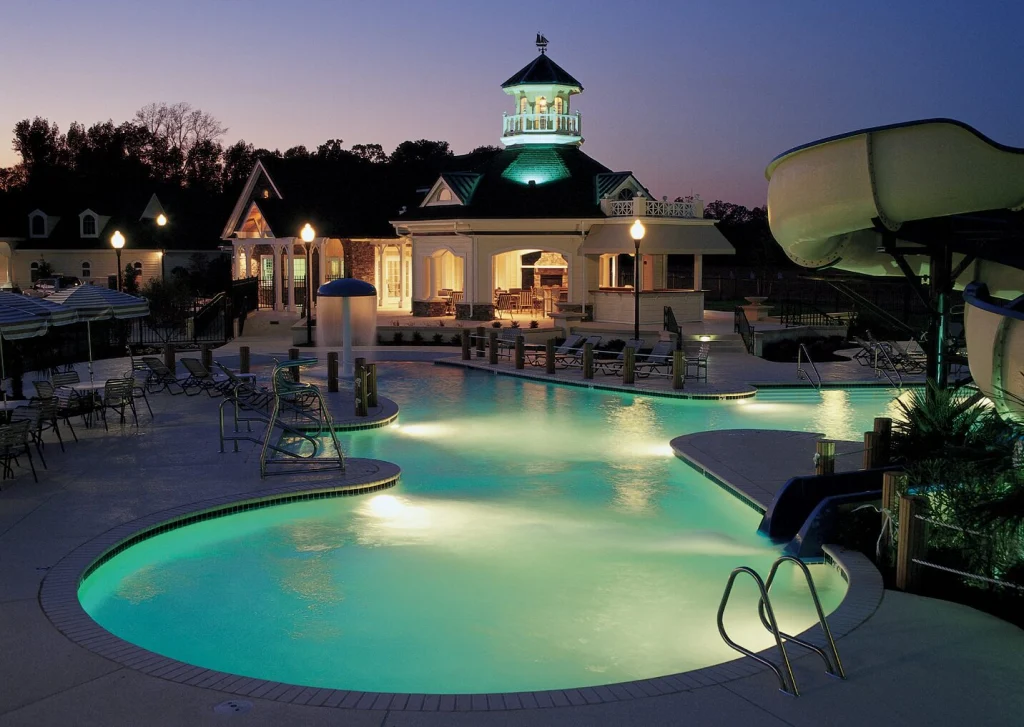 A resort pool glowing at dusk, with a waterslide and a clubhouse topped by a lit cupola